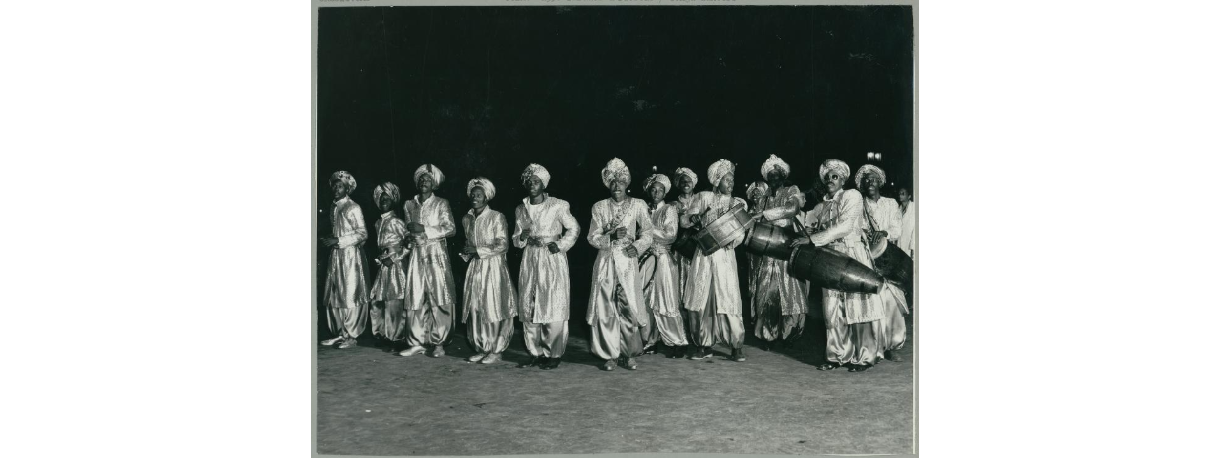 Black and white photo of a dozen Black men dancing Conga in Cuba.